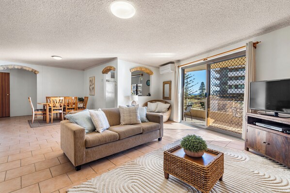 A spacious living area with a sofa, a TV, and a dining set.