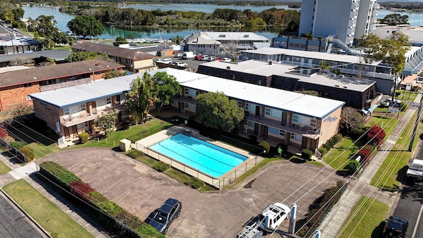 Un edificio de varios pisos con piscina, estacionamiento y vistas a un lago y montañas.