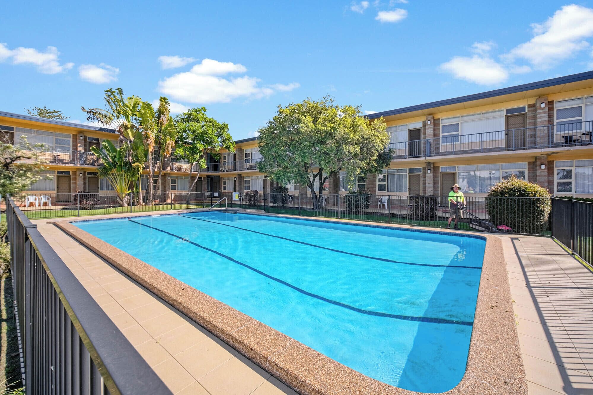 A rectangular swimming pool with a tiled edge, surrounded by a fence.