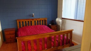 Un dormitorio con una cama de madera, una mesita de noche, un ventilador y una ventana con persianas.