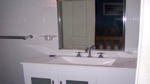 Un baño con un lavamanos blanco, dos llaves, un espejo y un perchero para toallas.