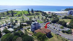 An aerial view of a coastal residential area with a prominent building marked by a red arrow. - Paradise Court 1 - Marina Views (Forster)