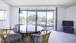 A dining area with a round table and chairs, a TV, and a sliding glass door leading to an outdoor patio. - Paradise Court 1 - Marina Views (Forster)