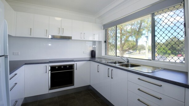 A modern kitchen with white cabinets, a stainless steel oven, a double sink, and a window with a view of the outside. - Paradise Court 1 - Marina Views (Forster)