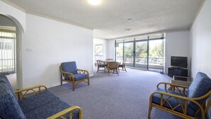 A spacious living area with wicker furniture, a dining table, and a television. - Paradise Court 1 - Marina Views (Forster)
