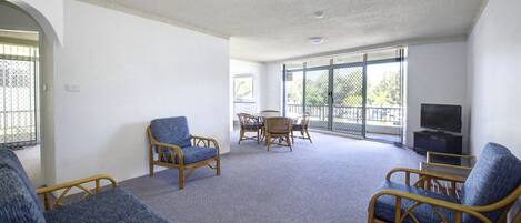 A spacious living area with wicker furniture, a dining table, and a television.