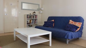 Une pi èce avec une table blanche, un canapé bleu avec des coussins, une bibliothèque et une porte.
