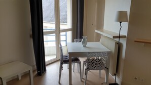 Une petite pièce bien éclairée, avec une table et des chaises blanches, un radiateur, une lampe et une vue sur l’extérieur par une fenêtre.