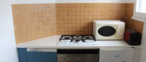 A compact kitchen with a gas stove, a microwave, a toaster, and a built-in oven.