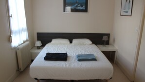 Un lit bien fait, avec une literie blanche et deux oreillers, une table de chevet avec une lampe et un tableau encadré au mur.
