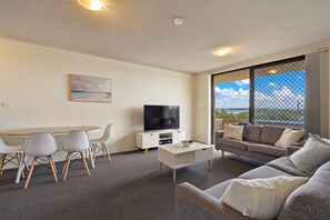 A modern living room with a flat-screen TV, a dining table with chairs, a sofa, and a large window with a view. - Lakeshore Lodge 2: 2  BR, 1  BA Apartment in Forster, Sleeps 4 (Forster)