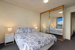 A bedroom with a large bed, two bedside tables with lamps, a full-length mirror, and a view through a window. - Lakeshore Lodge 2: 2  BR, 1  BA Apartment in Forster, Sleeps 4 (Forster)