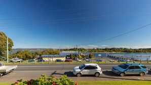Une route bordée de voitures garées, un bâtiment portant l’inscription « Paradise Motel », et une étendue d’eau en arrière-plan.
