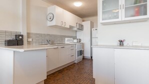 Une cuisine compacte avec des meubles blancs, un four à micro-ondes, une bouilloire et une horloge au mur.