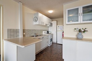 A kitchen with white cabinets, a clock, a microwave, a stove, and a refrigerator. - Lakeshore Lodge 2: 2  BR, 1  BA Apartment in Forster, Sleeps 4 (Forster)