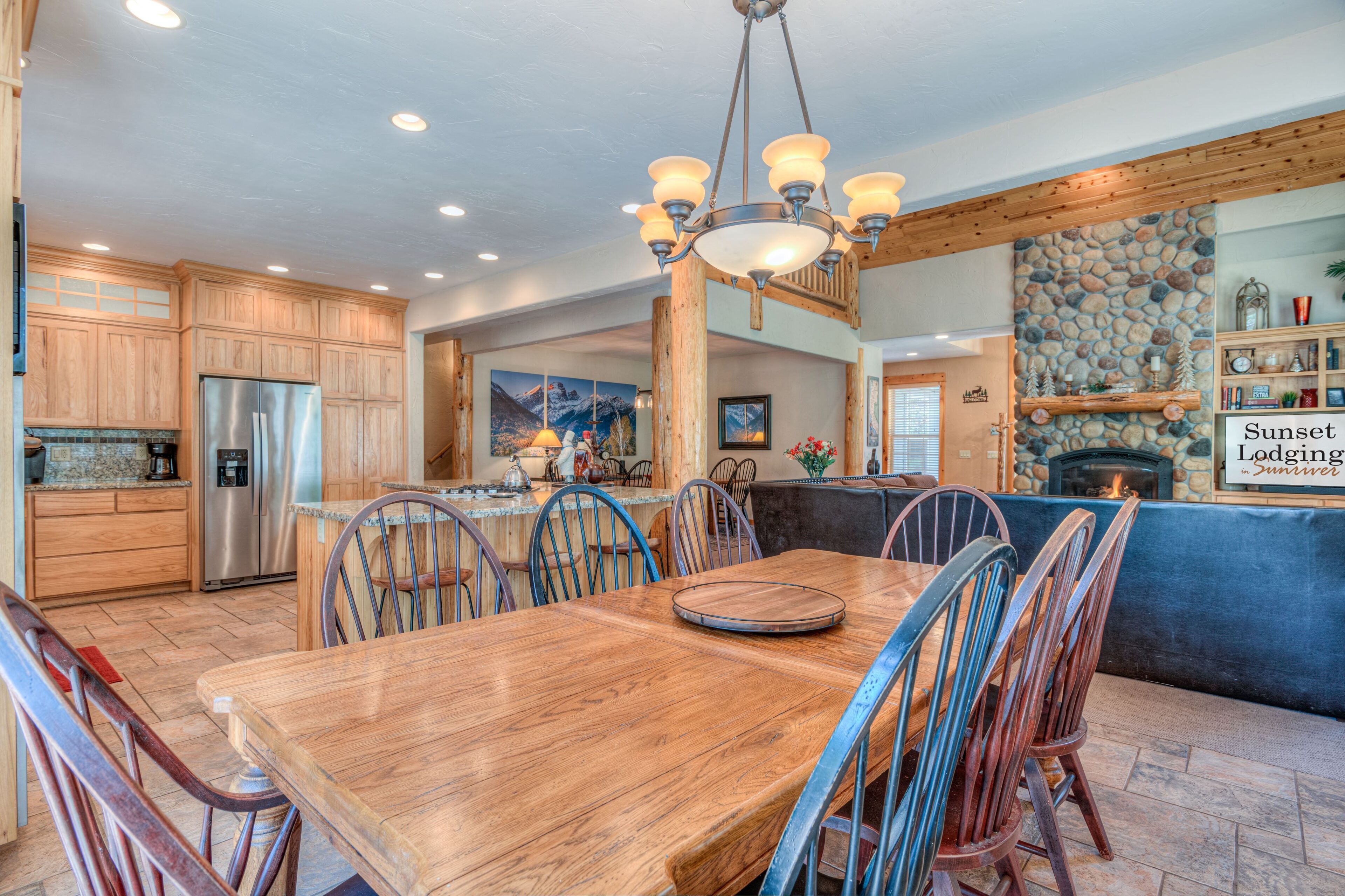 A spacious kitchen with wooden cabinets, a stainless steel refrigerator, and a dining area with a large wooden table and metal chairs.
