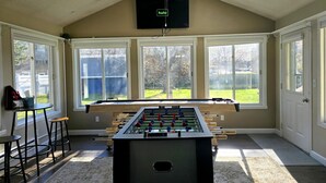 Une pièce équipée d’un baby-foot, de grandes fenêtres, d’un téléviseur et d’un coin bar.
