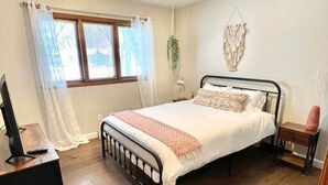 Une chambre à coucher avec un lit, un bureau, une fenêtre avec des rideaux, une plante fixée au mur et un luminaire au plafond.
