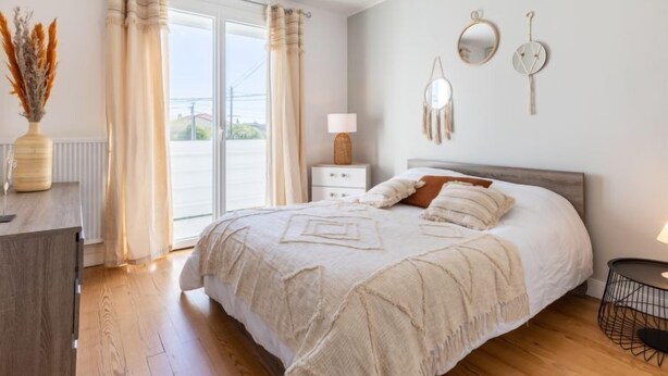 Ein Schlafzimmer mit einem großen Bett, einem Nachttisch, einer Lampe und Blick ins Freie durch eine Schiebetür.