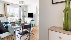 Ein modernes Wohnzimmer mit Essbereich, einem Fernseher und einer grünen Vase auf einem Schrank.
