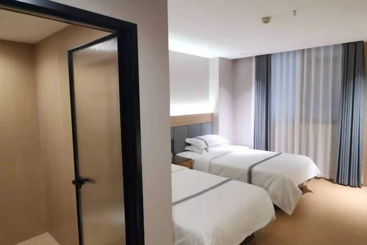 Una habitación de hotel con dos camas, un cabecero, una ventana con cortinas y una puerta.