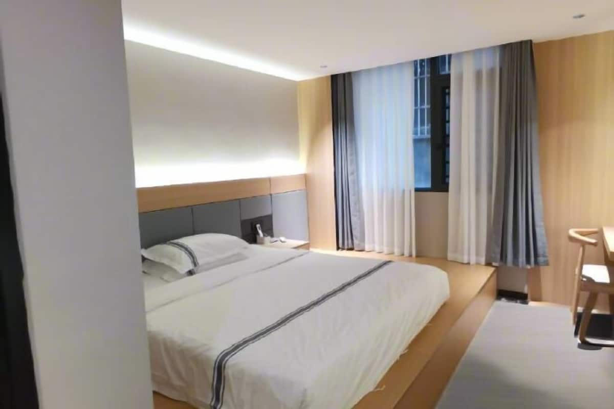 Una habitación de hotel moderna con una cama grande, una mesita de noche, un escritorio y una ventana con cortinas.