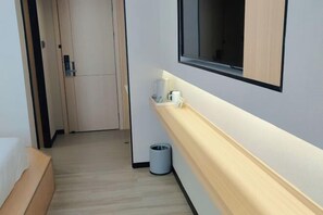 Habitación de hotel con una cama, una mesita de noche pequeña, un cesto de basura, un estante en la pared con una cafetera y una ventana.