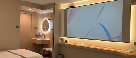 A hotel room with two beds, a large mirror, a vanity with a sink, and a wall-mounted TV.