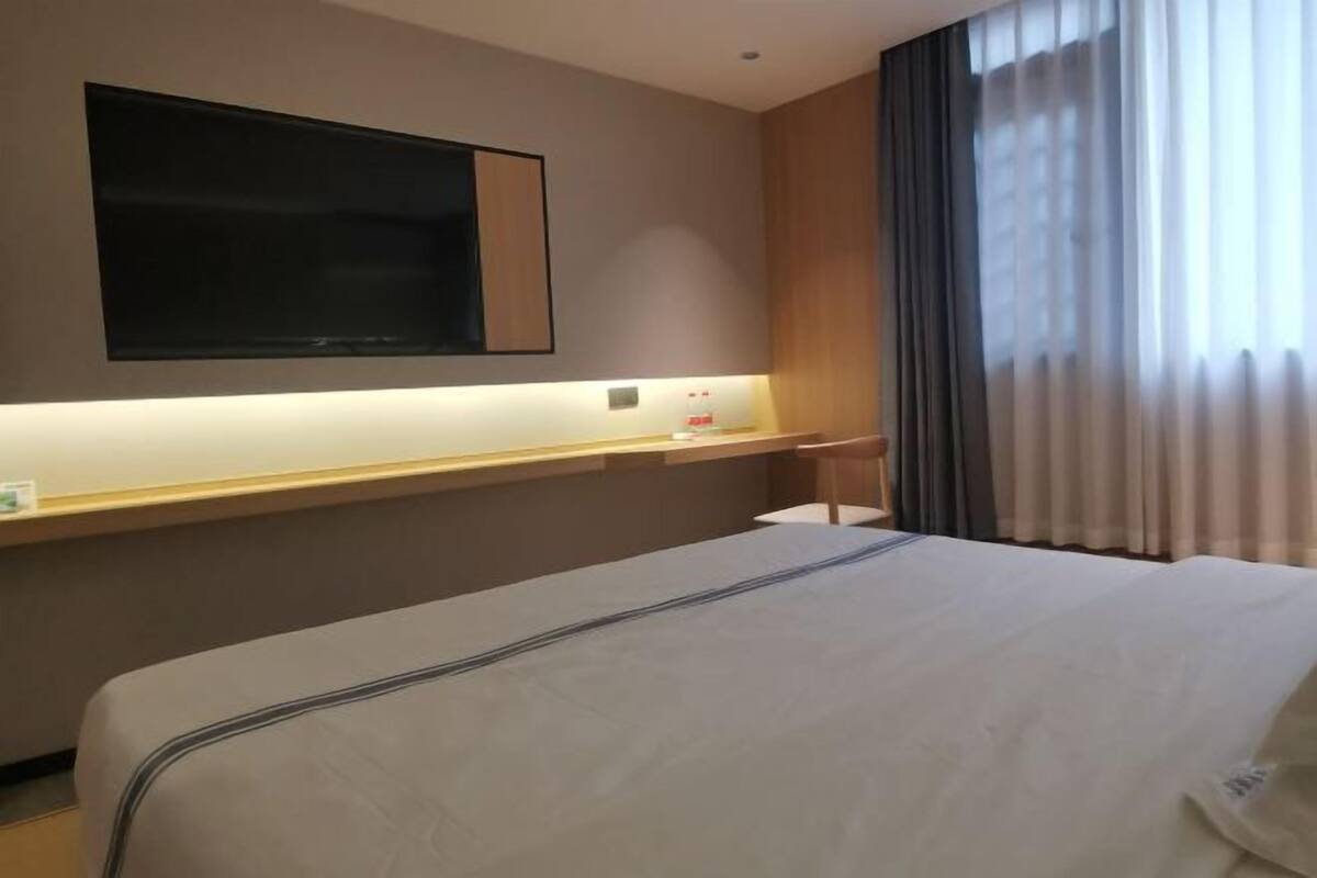 Habitación de hotel con cama, escritorio, televisor montado en la pared y ventana con cortinas.