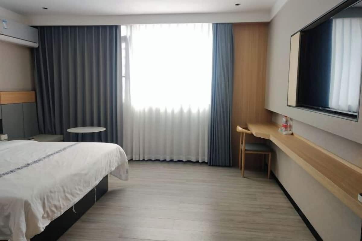Una habitación de hotel con cama, escritorio, silla, televisor y ventana con cortinas.