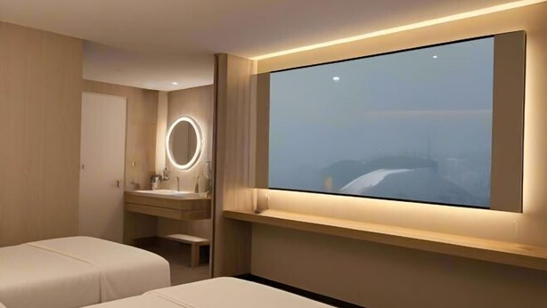 Habitación de hotel moderna con una televisión grande, una mesita de noche, un espejo y vistas a un paisaje montañoso.
