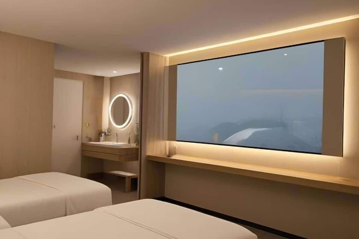Habitación de hotel moderna con una televisión grande, una mesita de noche, un espejo y vistas a un paisaje montañoso.