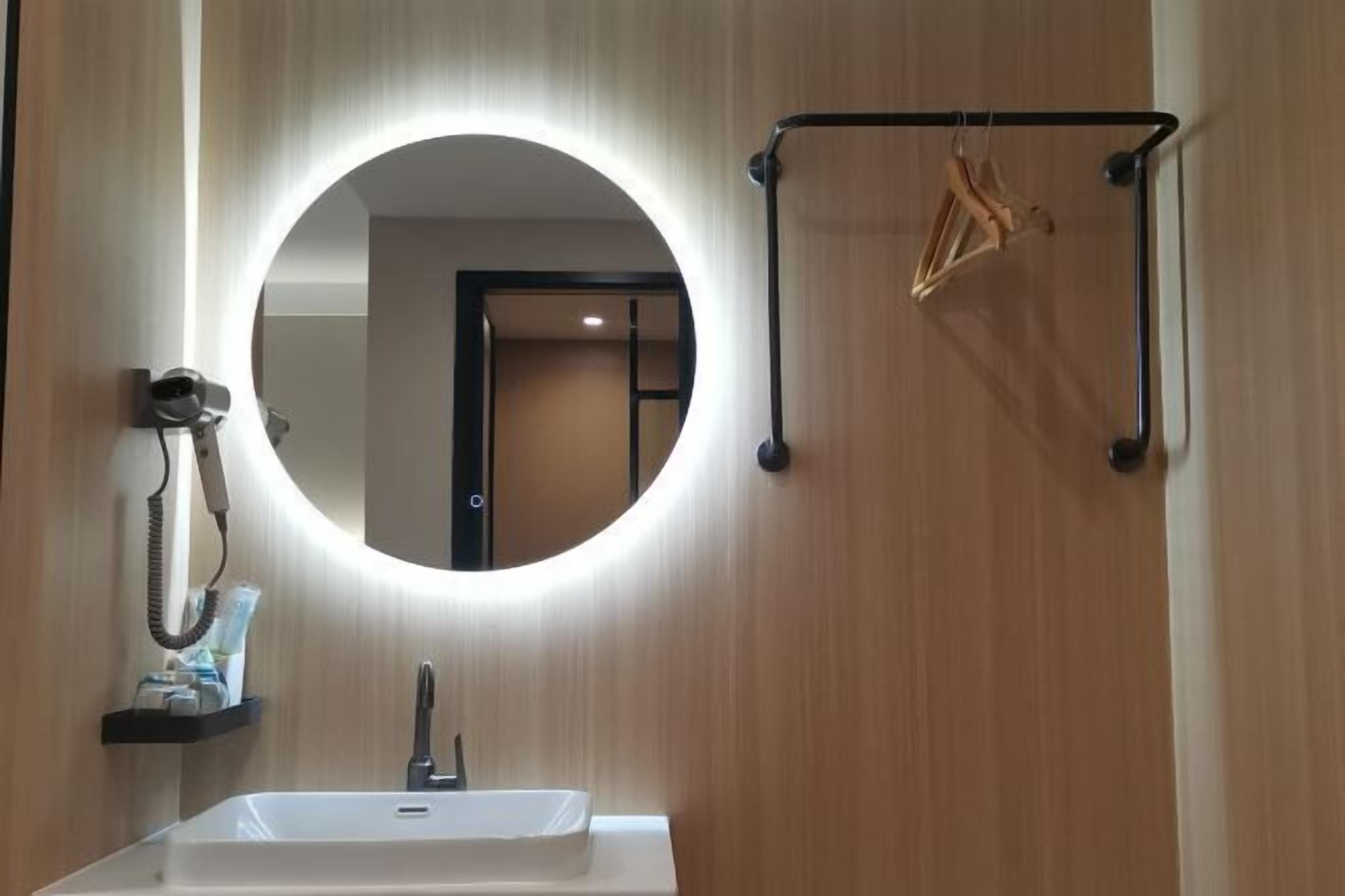 Casa de banho com espelho redondo, lavatório e toalheiro com cabides.
