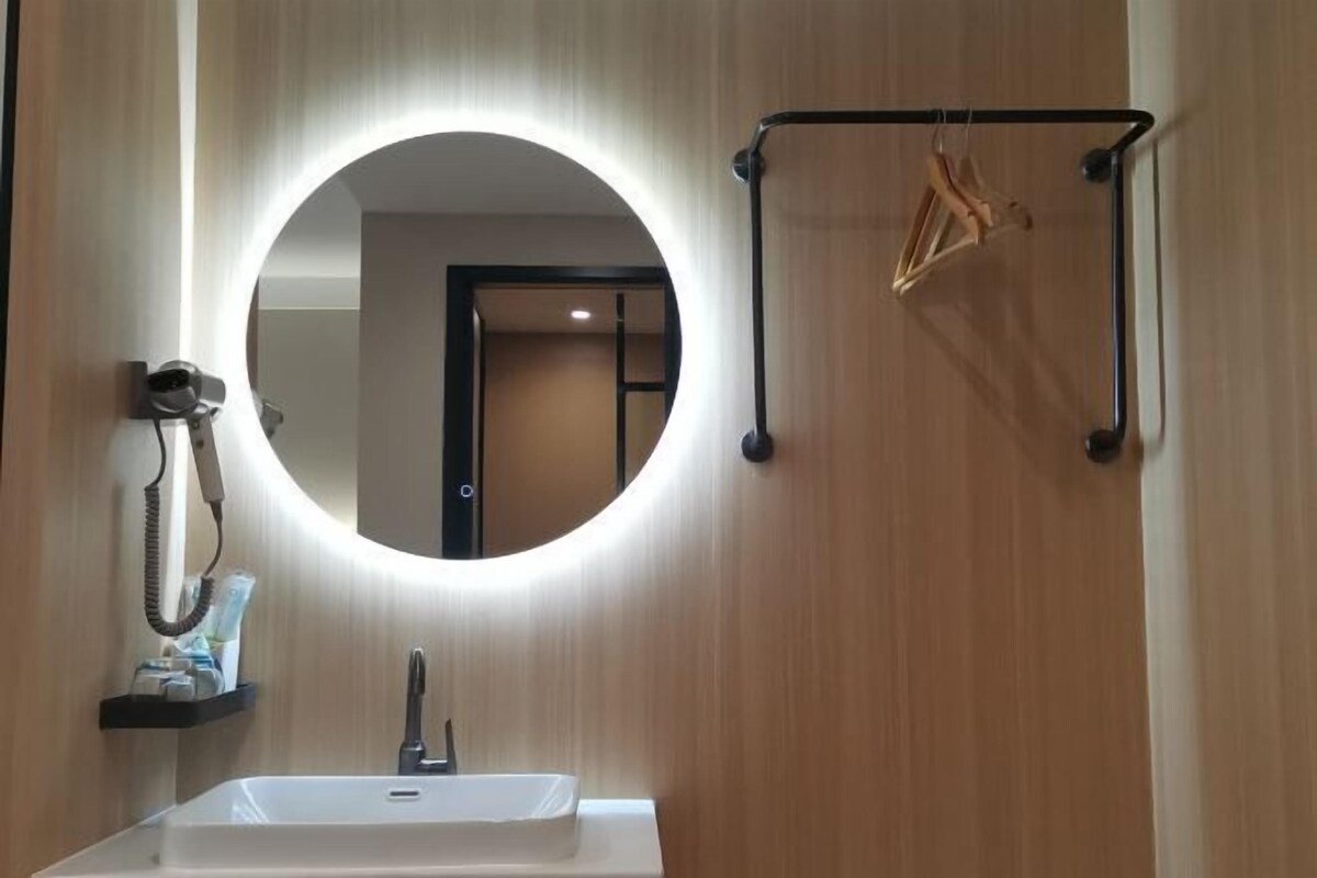 A bathroom with a round mirror, a sink, and a towel rack with hangers.