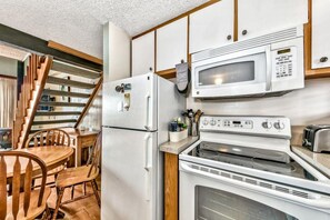 Une cuisine compacte équipée d’un réfrigérateur, d’un four à micro-ondes, d’une cuisinière, ainsi que d’un coin repas avec des chaises et une table en bois.