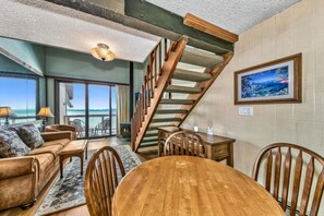 A cozy living room with a wooden staircase, a dining table, and a large window overlooking a scenic view. - Beach Front Condo, Views, Views Views (South Lake Tahoe)