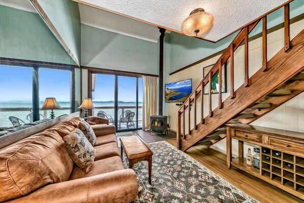 A spacious living room with a large sofa, a wooden staircase, and a view of the sea.