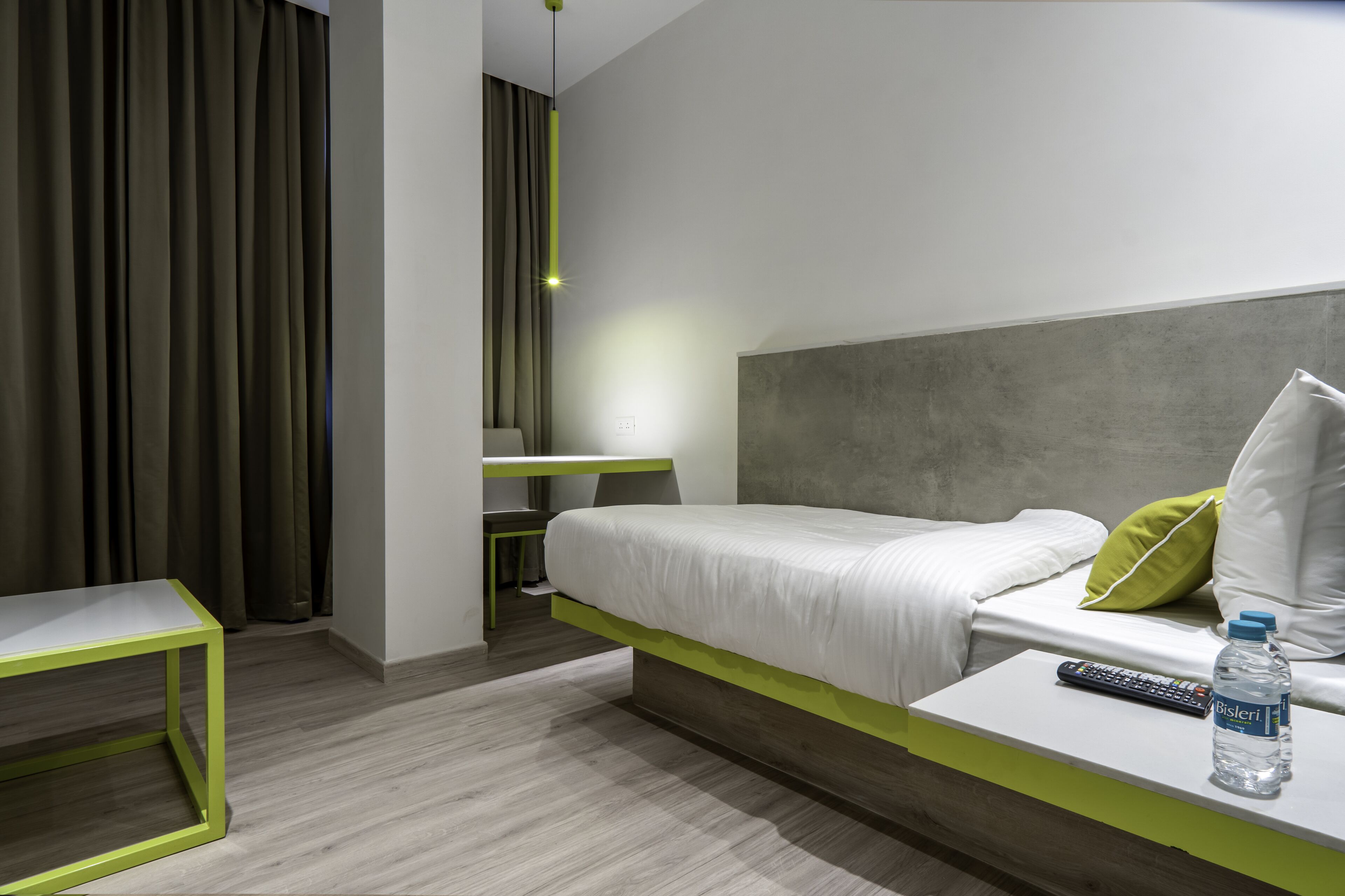 Een moderne hotelkamer met een bed, een bureau, een stoel en een waterfles op het nachtkastje.