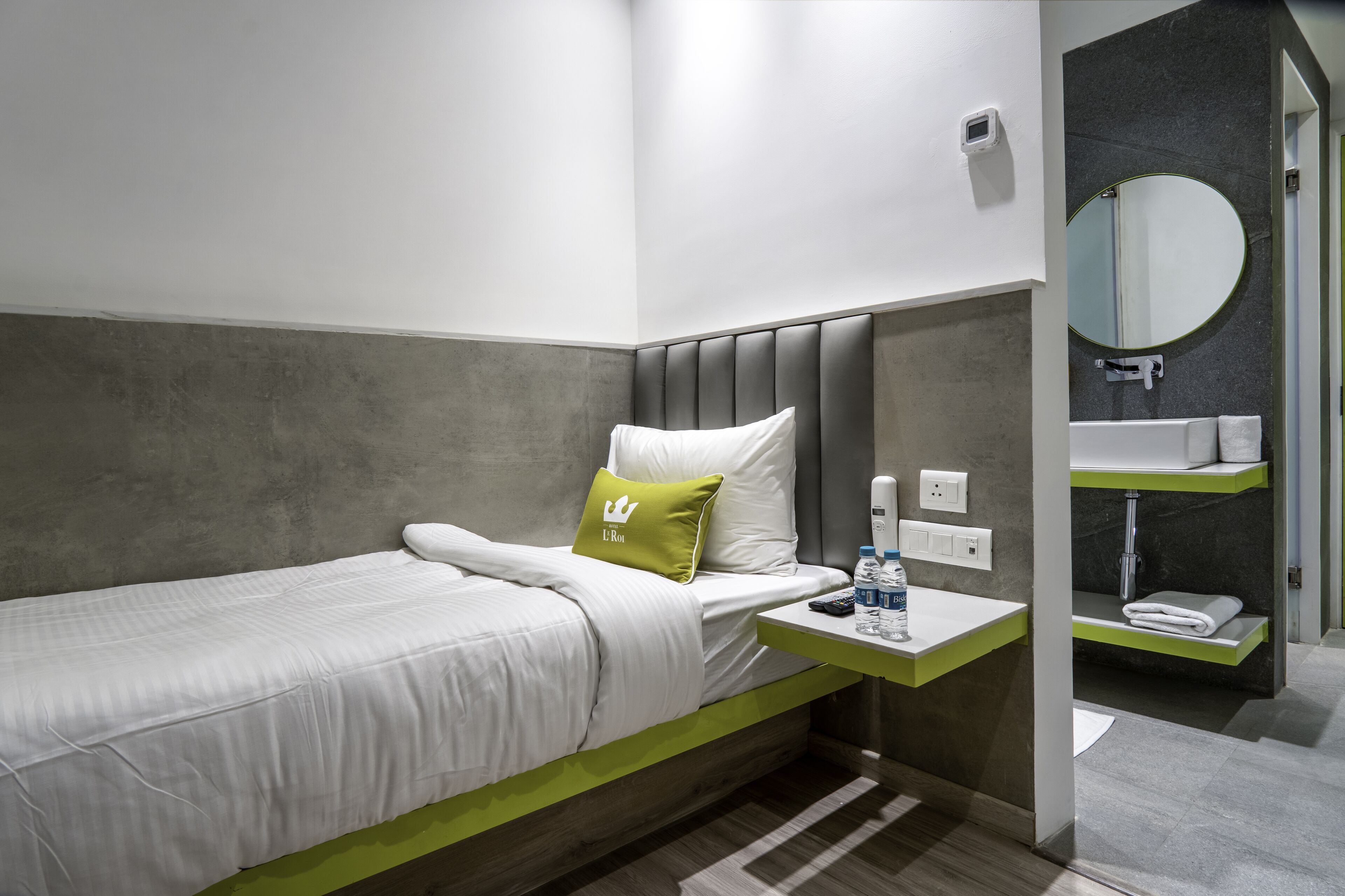 A hotel room with a bed, a bedside table with a bottle, a pillow, and a mirror.