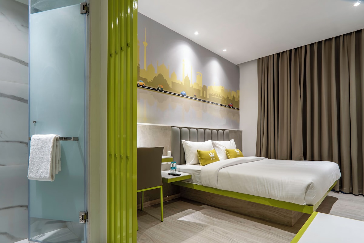 A modern hotel room with a bed, bedside table, and a shower area.