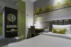 Habitació d'hotel amb un llit, una taula de treball, una cadira, un mirall, una estant amb articles de tocador i un mural a la paret.