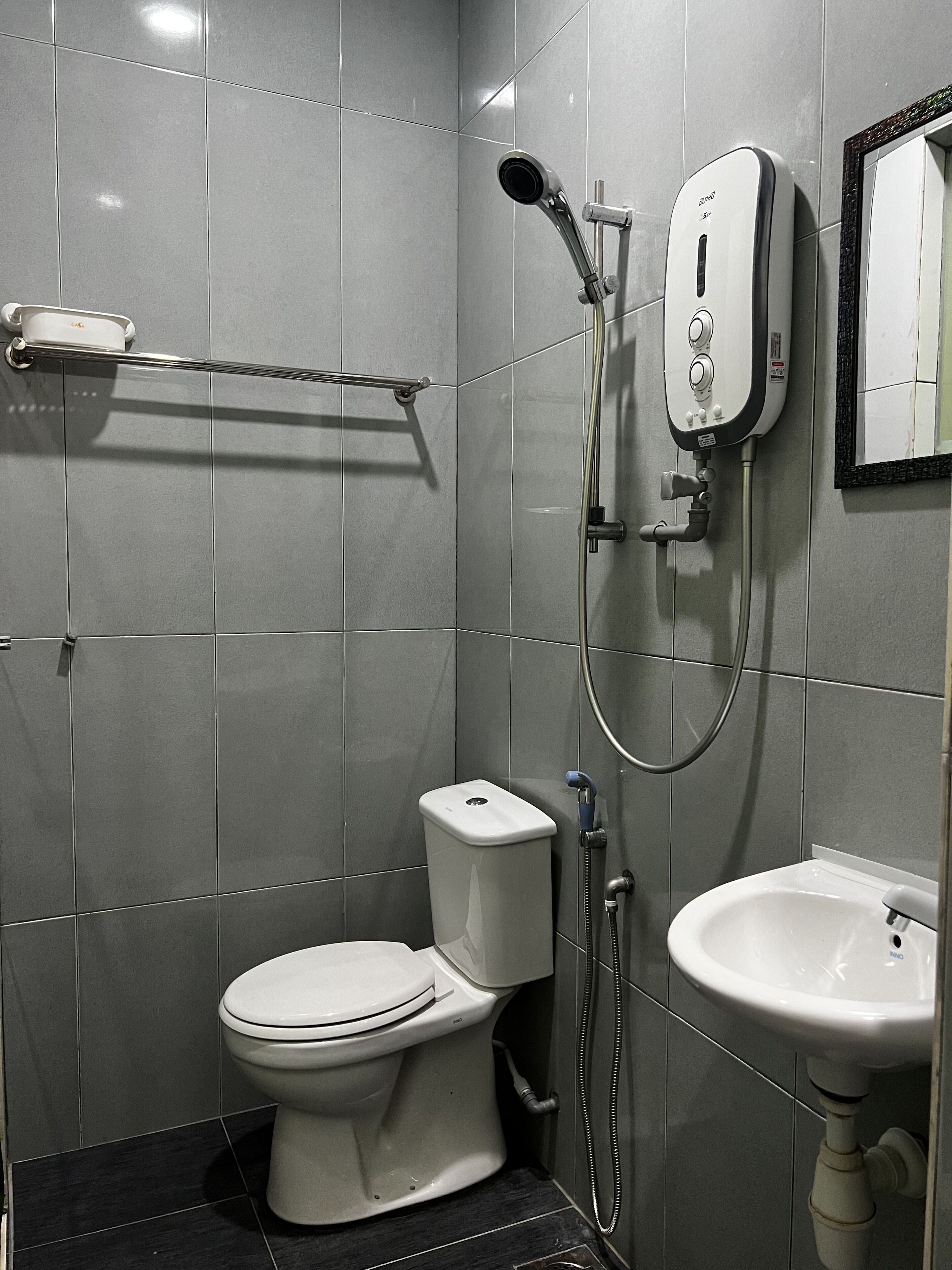 A modern bathroom with a toilet, a shower with a handheld showerhead, and a sink.