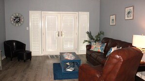 Uma sala de estar com um sofá de couro marrom, uma mesa de centro azul, uma poltrona preta e um relógio na parede.