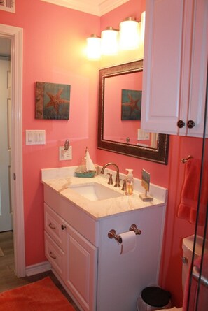 Un baño con paredes rosadas, un tocador blanco con lavabo, un espejo y un perchero para toallas.