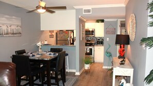 Uma sala de jantar com mesa e cadeiras, uma cozinha equipada e um corredor que dá para outro quarto.
