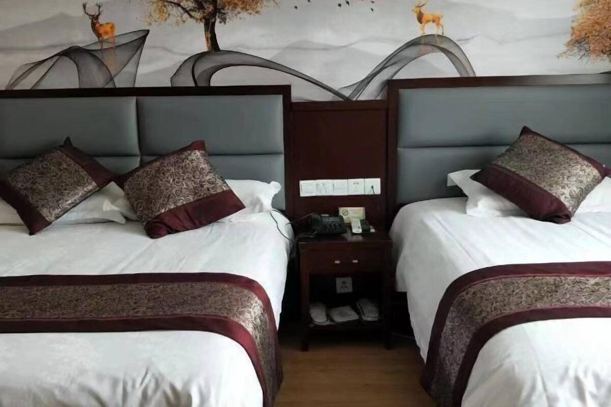 Hotellihuoneessa on kaksi sänkyä, joissa on molemmissa kuviollisia tyynyjä ja pääty. Sänkyjen välissä on yöpöytä, jossa on puhelin ja pieni pöytä.