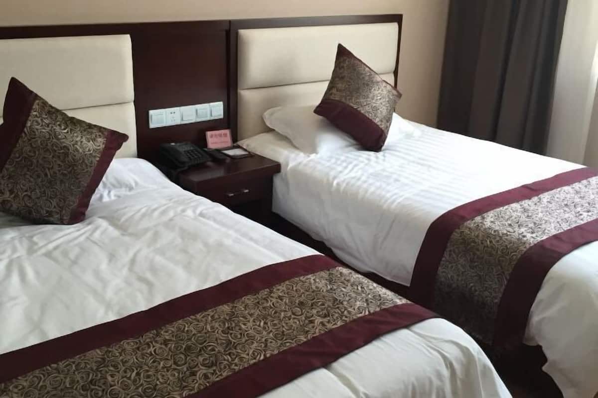 Hotellihuone, jossa on kaksi sänkyä, ja jokaisessa sängyssä on pääty. Lisäksi huoneessa on yöpöytä, jossa on puhelin ja lamppu, sekä seinälle asennettu ohjauspaneeli.