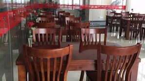 Un comedor con mesas y sillas de madera, un separador de vidrio y un cartel rojo.