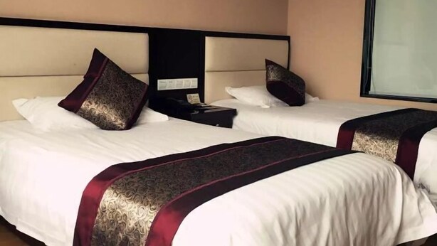Habitación de hotel con dos camas, cada una con ropa blanca y almohadillas decorativas rojo oscuro.