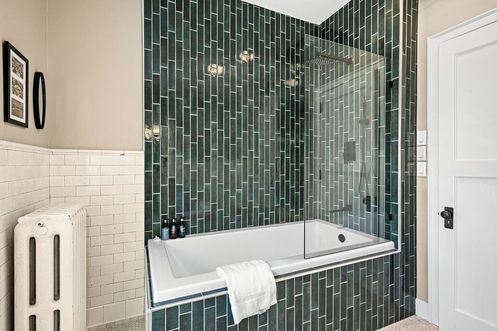 A modern bathroom with a glass-enclosed shower, a white bathtub, and a white radiator.